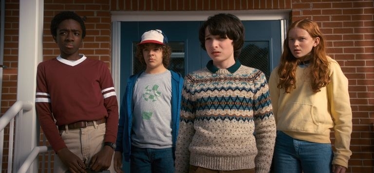 Lucas, Dustin, Mike and Max stand in front of a brick building looking confused