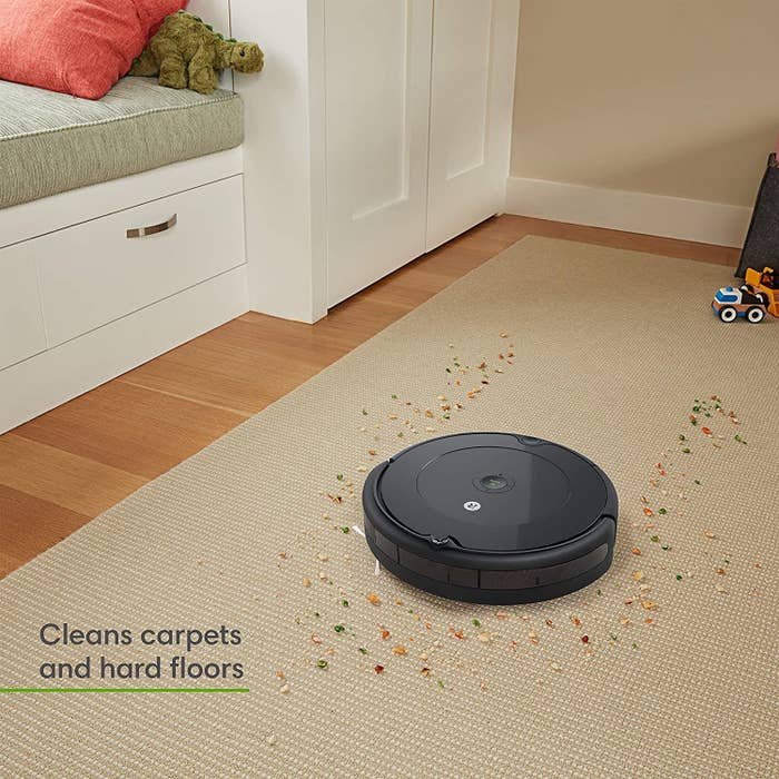 The black roomba vacuuming up a carpet, with text that it cleans carpets and hard floors