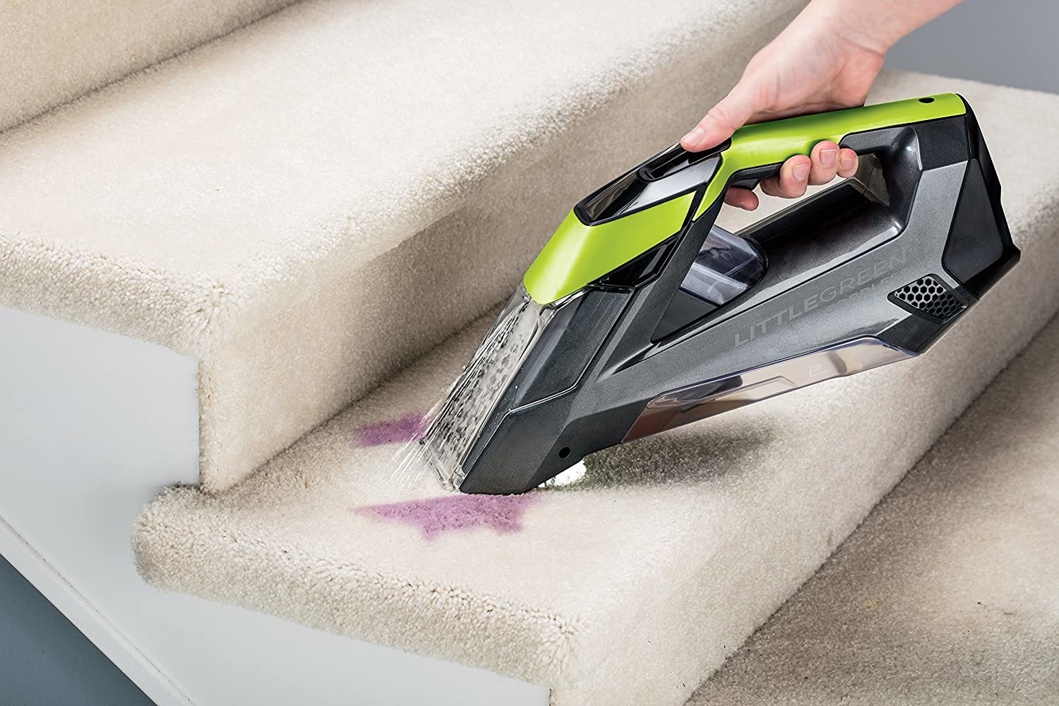 A handheld vaccuum getting rid of a dark carpet stain