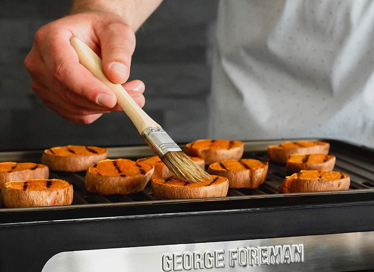 A person brushes sweet potatoes on a grill