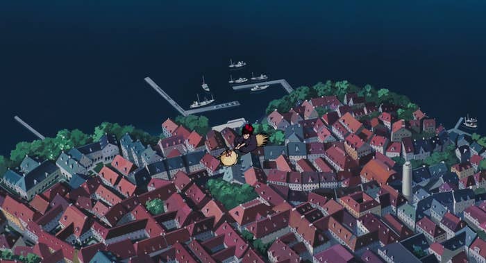 A still of an animated witch flying over a seaside town