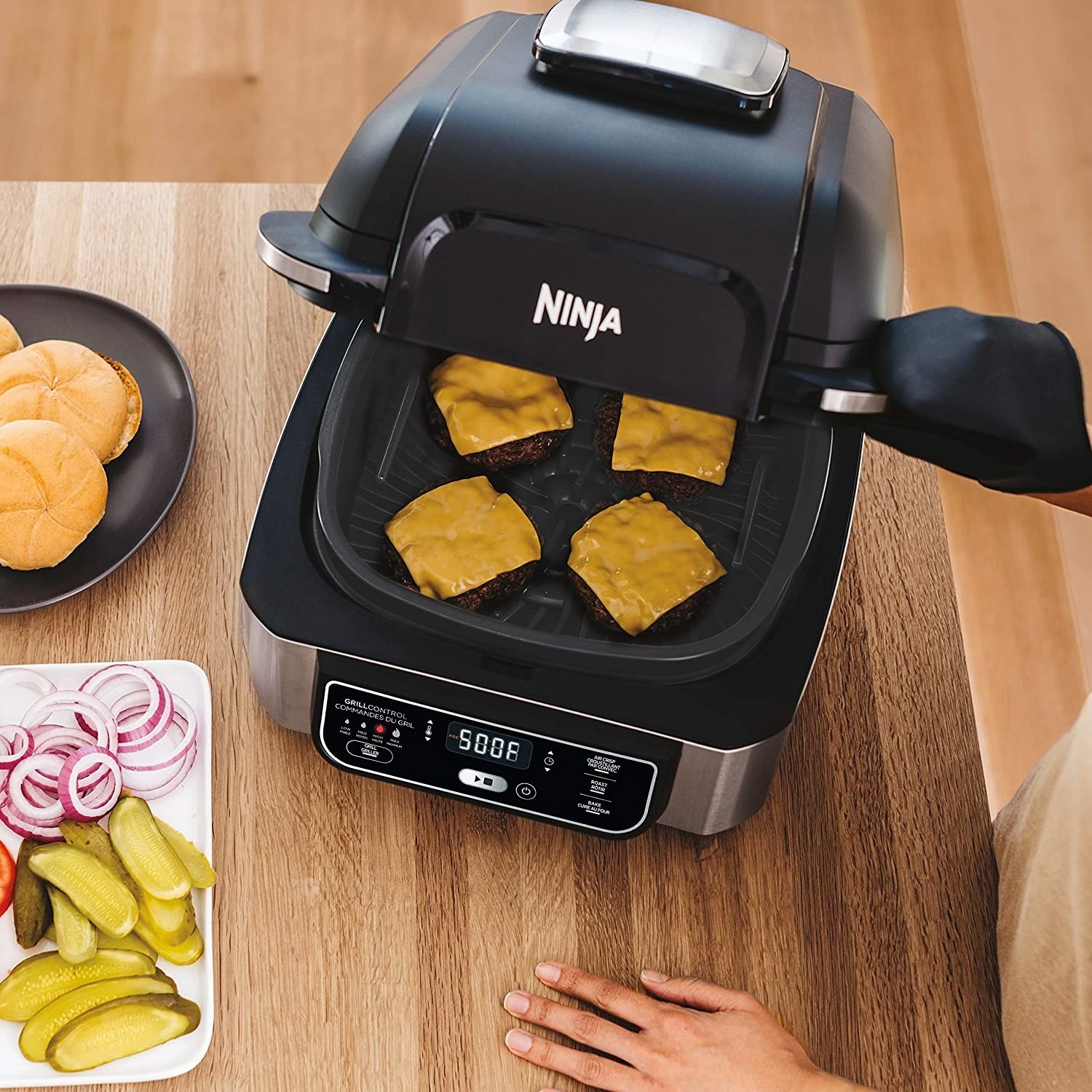 A person grilling four burgers with cheese on the grill