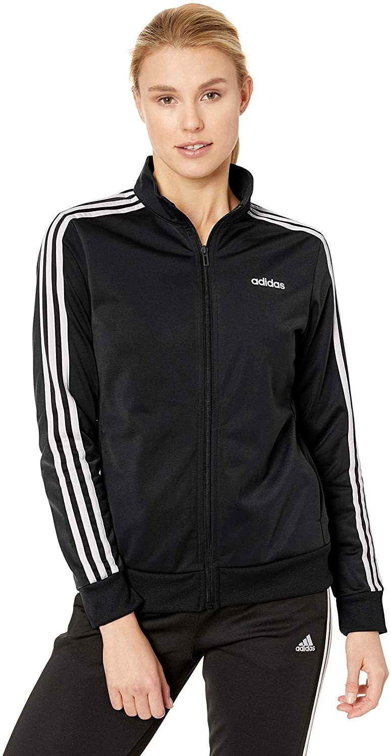 Model in the black zip-front jacket with adidas logo on front corner and white stripes down the sleeves