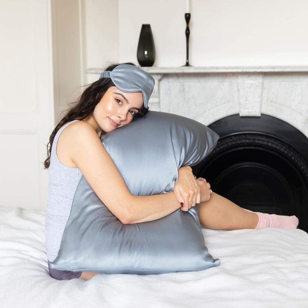 A person in bed holding a pillow with a soft silk pillowcase on it