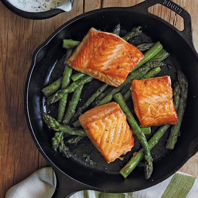 The black skillet with a long handle and a second helper handle with salmon and veggies inside 
