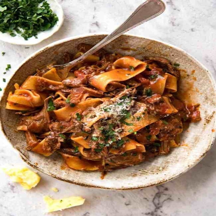 A bowl of tagliatelle with shredded beef ragu, Parmesan, and basil.