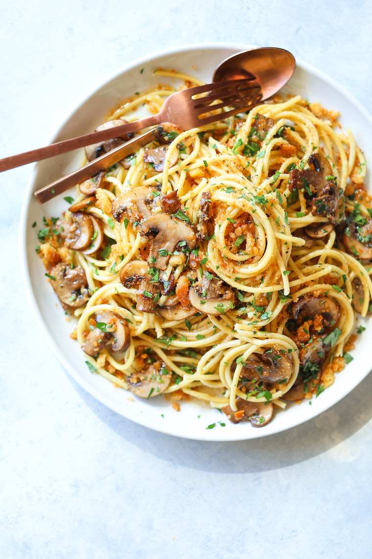 A plate of spaghetti with mushrooms, crispy bacon, and fresh herbs.