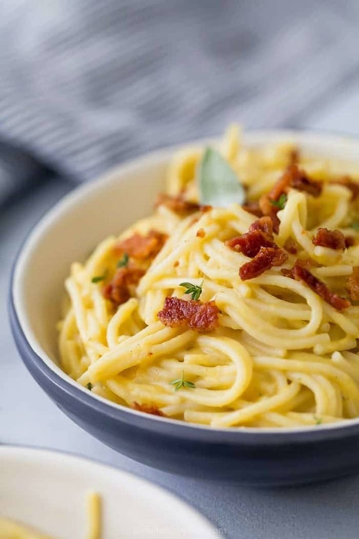A bowl of spaghetti in butternut squash sauce with bacon bits.