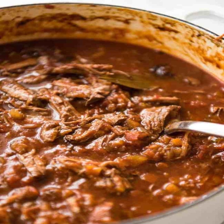 A Dutch oven filled with shredded beef ragu in tomato sauce.