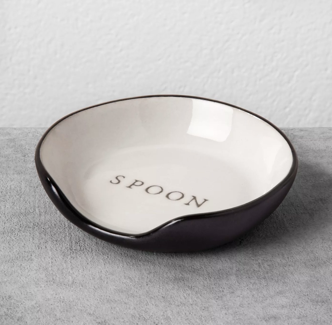 a white porcelain spoon rest with black trimming and the word &quot;spoon&quot; etched into the base