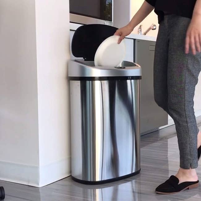 A model throwing trash into the stainless steel trash can with the lid popped open 