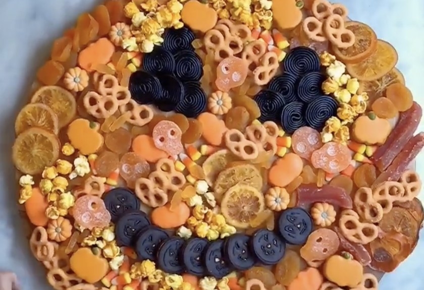 A board of food filled with cookies and pretzels that look like a pumpkin