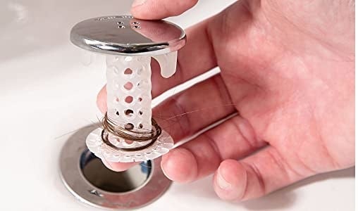 hand holding the clear SinkShroom with a silver top that looks like a bathroom drain