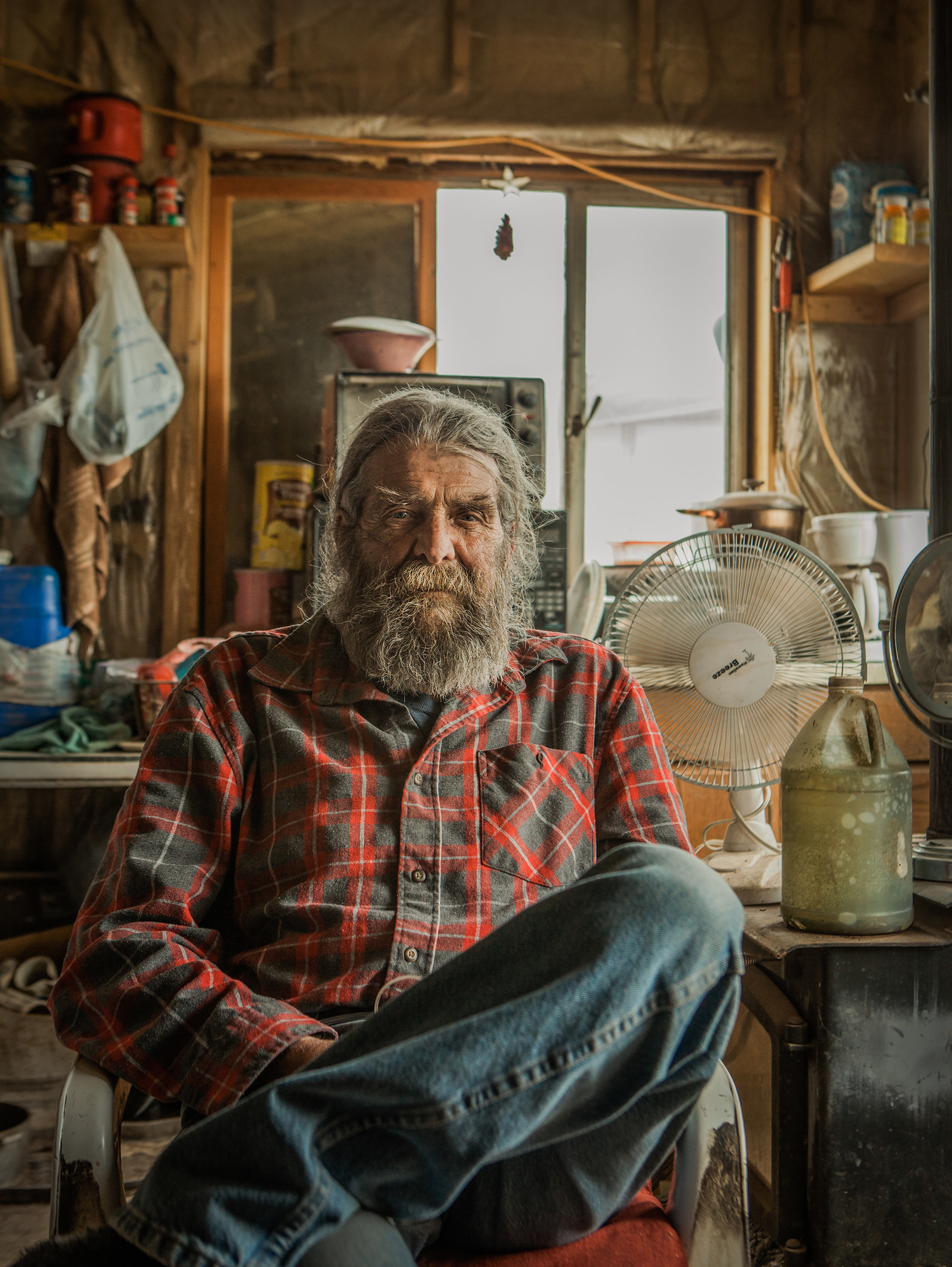 An old man with a beard wearing flannel in a cabin 