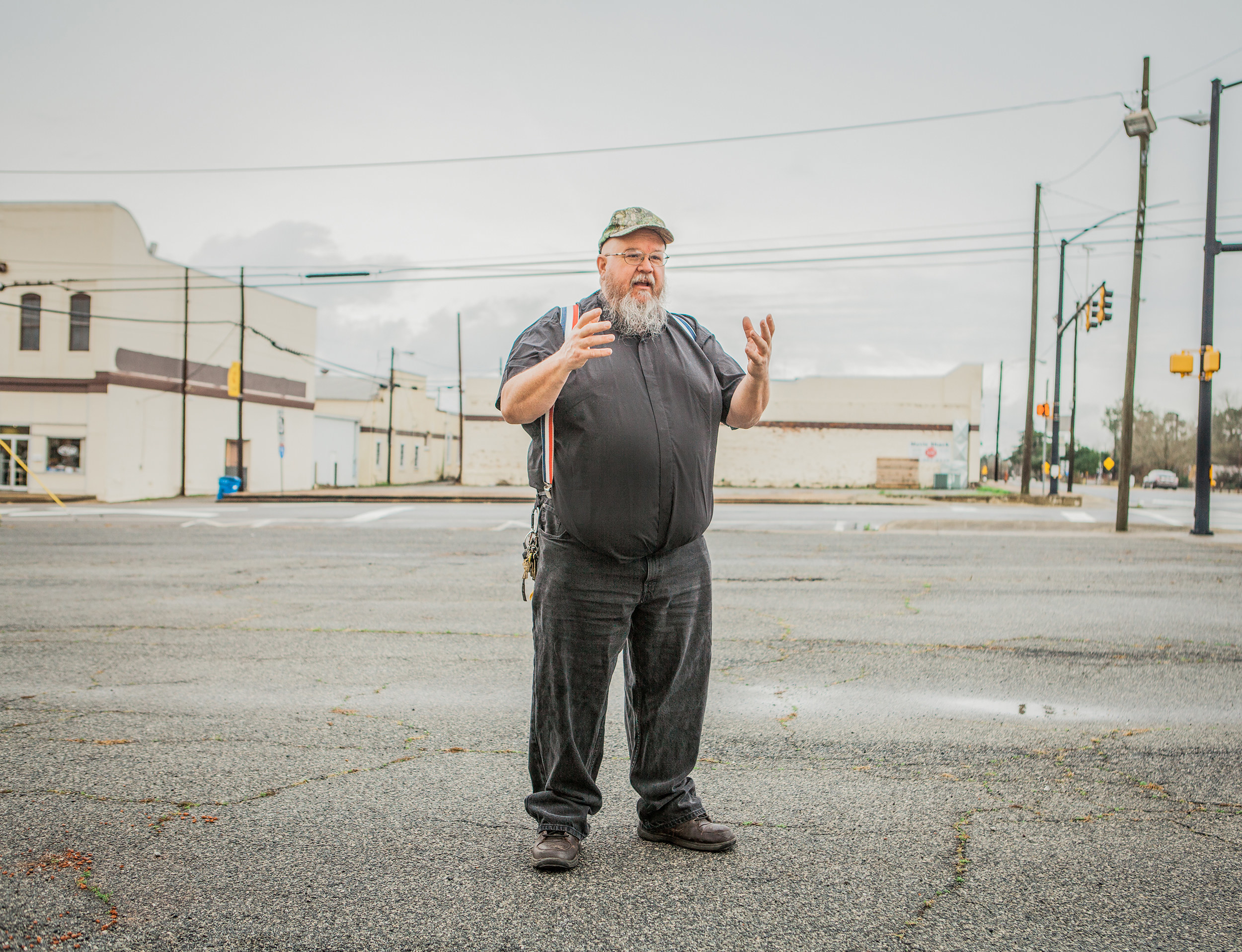 An older man in jeans and suspenders in a parking lot