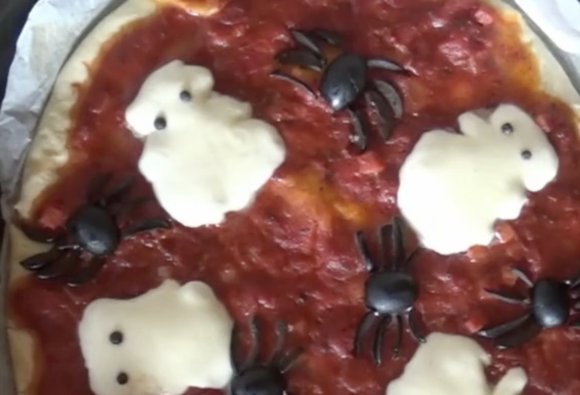 A pizza with cheese shaped like ghosts and olives shaped like spiders