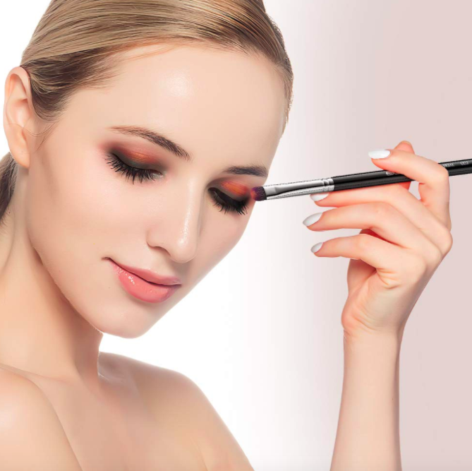 Model holds black angled makeup brush to apply eyeshadow to their eyes