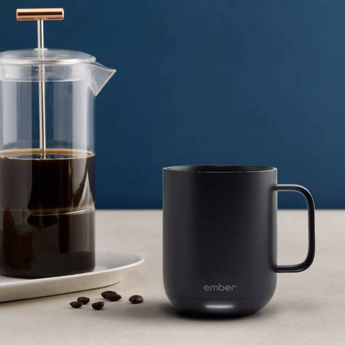a black ember mug with an LED light at its base sitting next to a french press