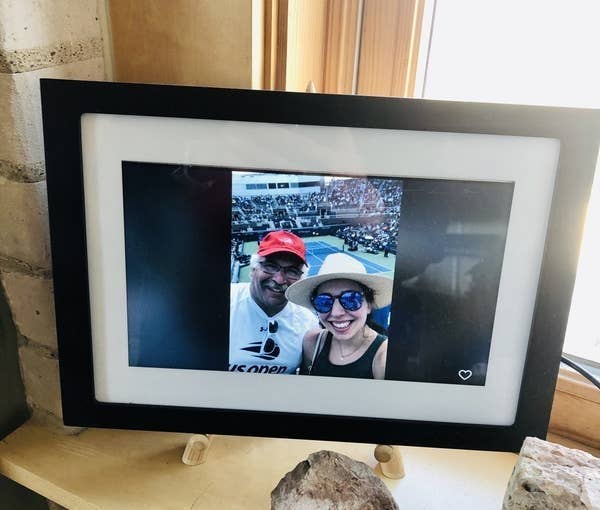The frame with a white and black frame around the digital screen in the author's parent's home with a picture of her and her father at a tennis match