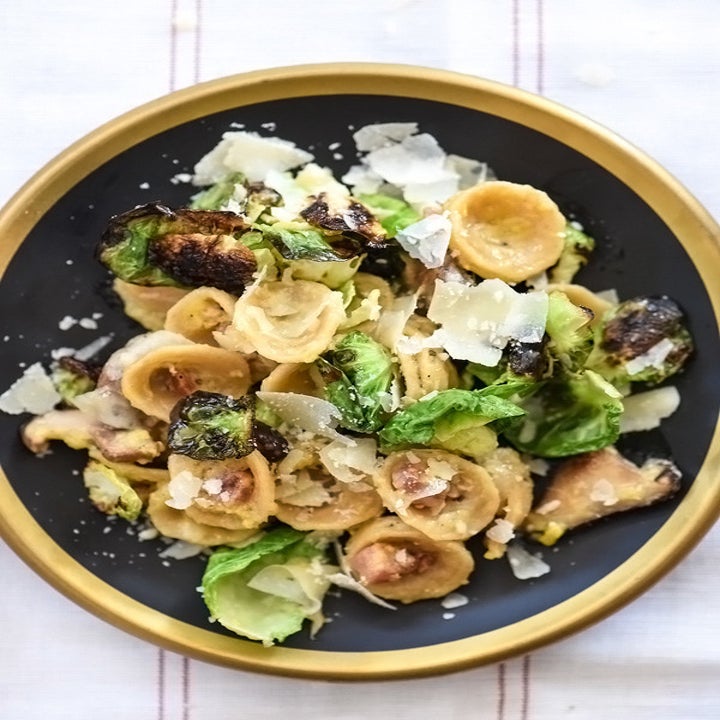 A bowl of orecchiette with Brussels sprouts, mushrooms, and Parmesan flakes.