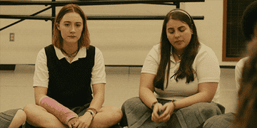 Two high school girls in uniform sitting on the floor while one breaks down