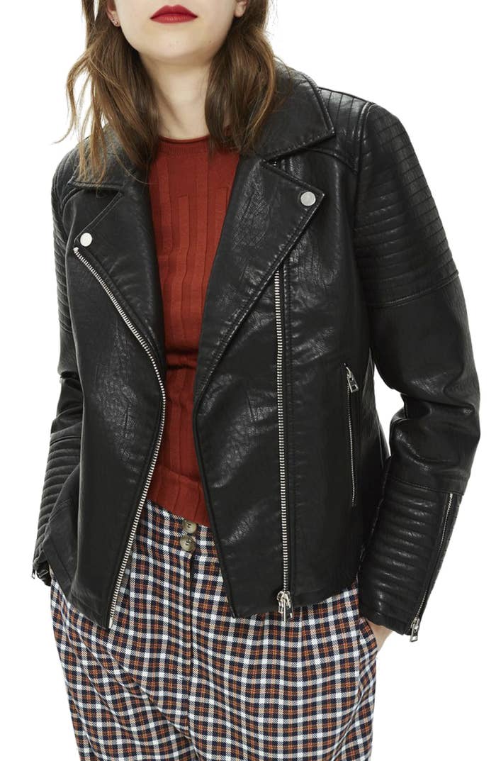 model wearing the leather jacket which has a silver asymmetrical zipper down the front, lapels, and zippers on each sleeve
