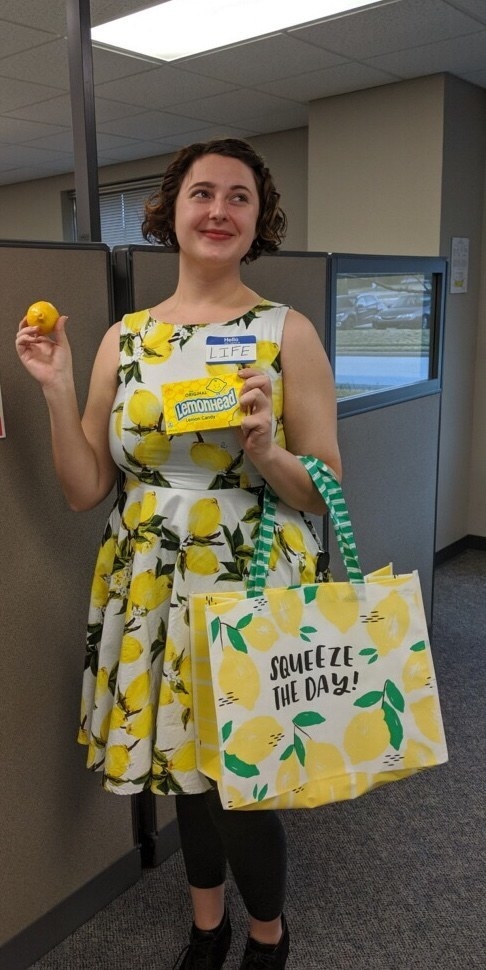 A woman in a lemon dress and a name tag reading &quot;hello, my name is life&quot; who is handing out lemons and lemonhead candy