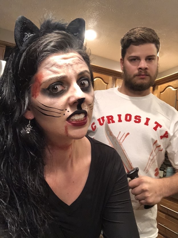 A woman dressed as a bloody cat and a man with a knife wearing a shirt that says &quot;curiosity&quot; 