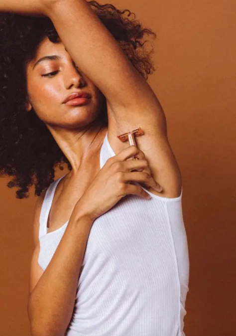 Model holds rose gold razor against armpit while shaving