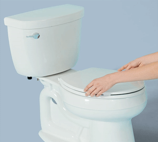 Hands place white Tushy bidet attachment on white toilet