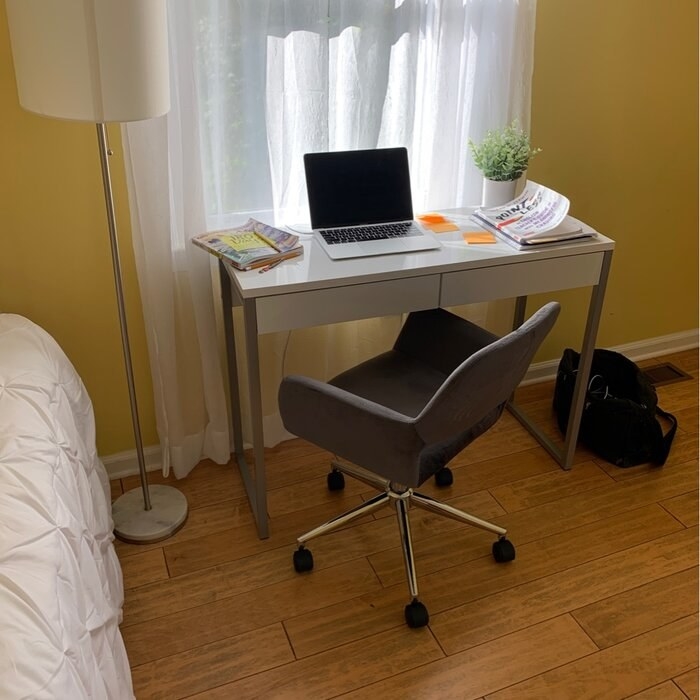 The white version of a desk holding a laptop, a book, a plant with a small task chair pulled up