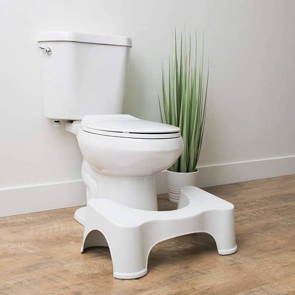 The Squatty Potty sitting on the floor in front of a toilet, like a stool