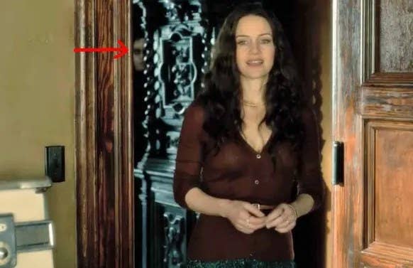 The Haunting of Hill House still: Olivia Crain stands in a doorway; a red arrow points to a ghostly face that lurks in the background behind her