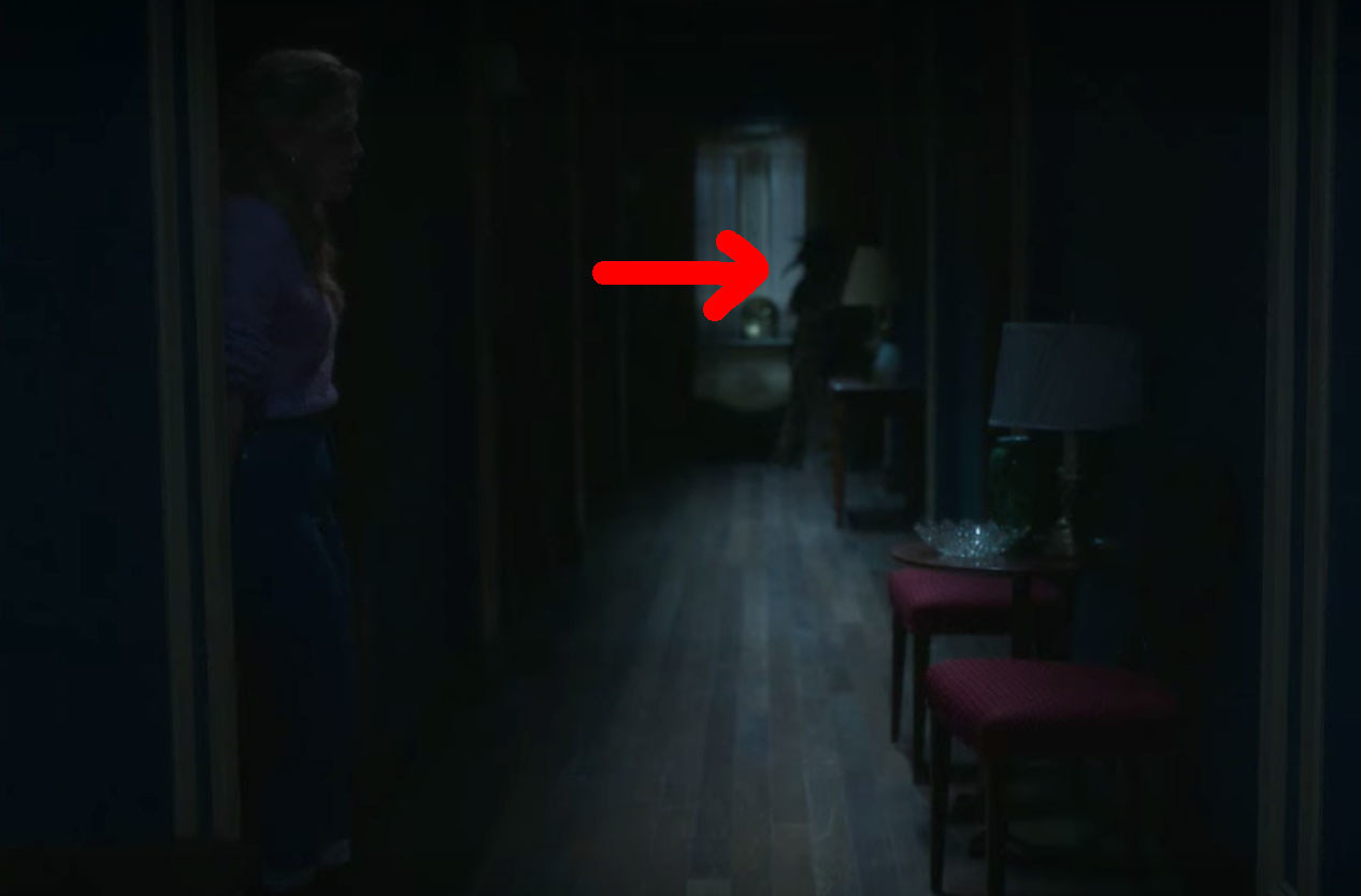 Dani exits Flora&#x27;s room; at the end of the hallway a red arrow points to the silhouette of the plague doctor