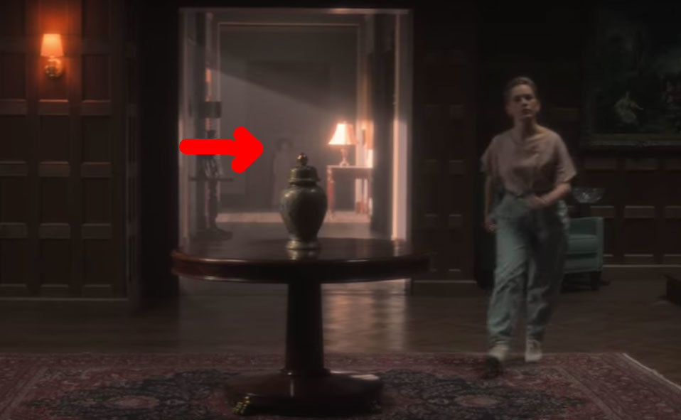 Dani moves through the foyer of Bly Manor; a red arrow points to a ghost child in the background behind her