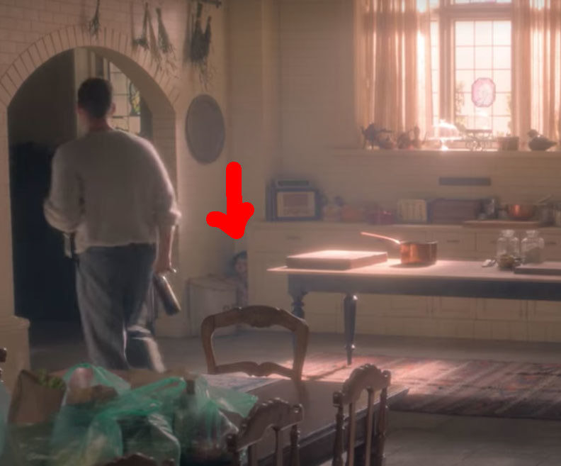 Peter walks out of the kitchen; near him a red arrow points to a doll-faced figure crouched in the corner