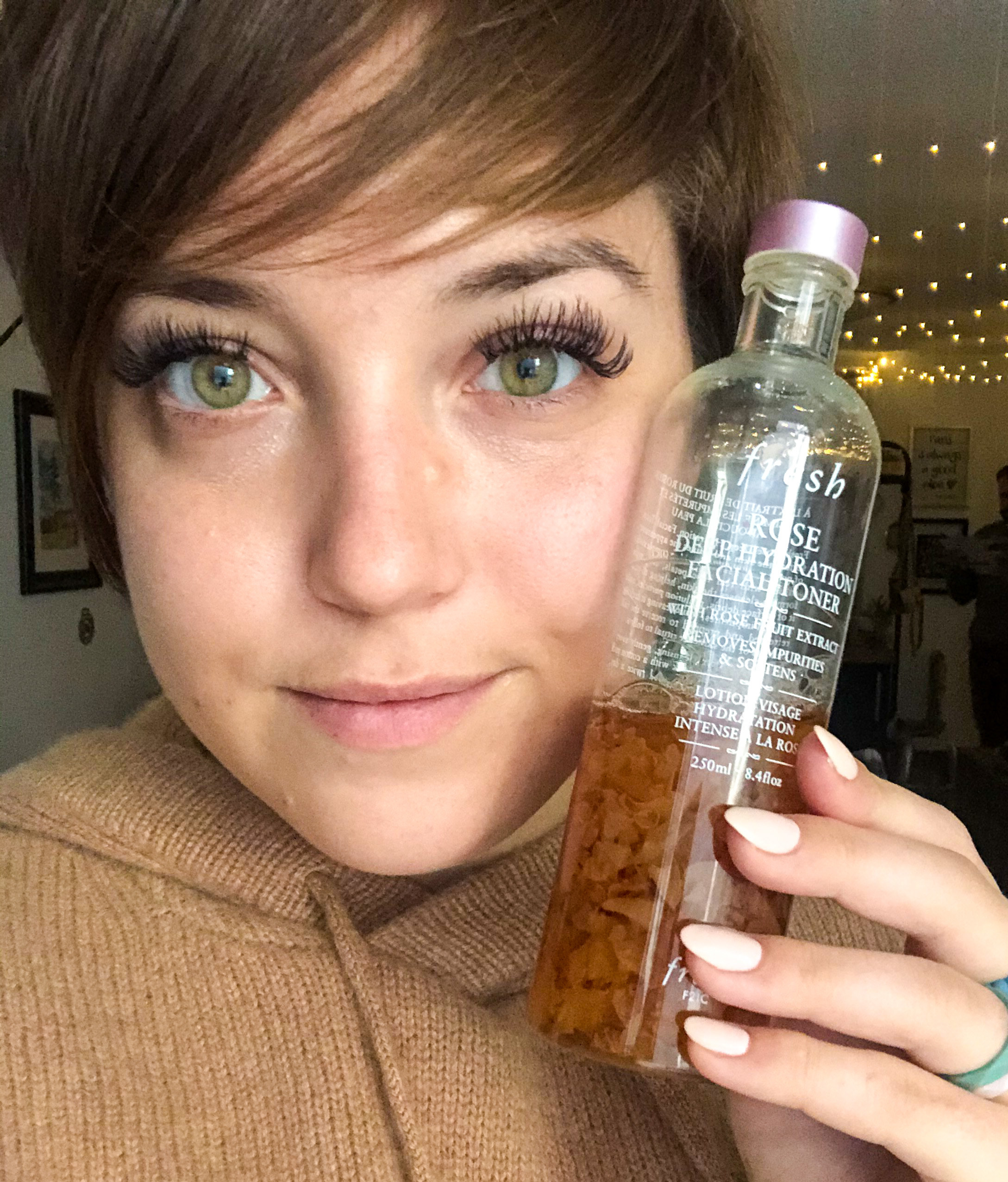 A person holds a half-empty bottle of the toner against their face