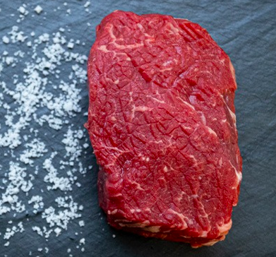 An uncooked piece of steak beside a tabletop of salt 