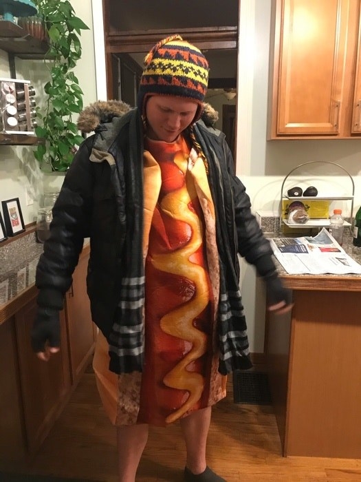 A person in a hot dog costume with two winter jackets and a beanie over it