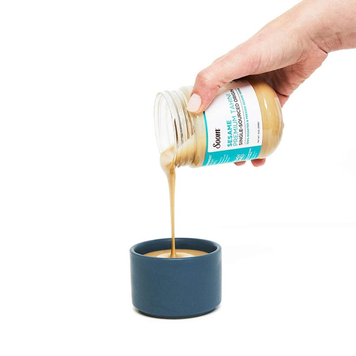 Someone pouring Soom tahini into a small bowl.