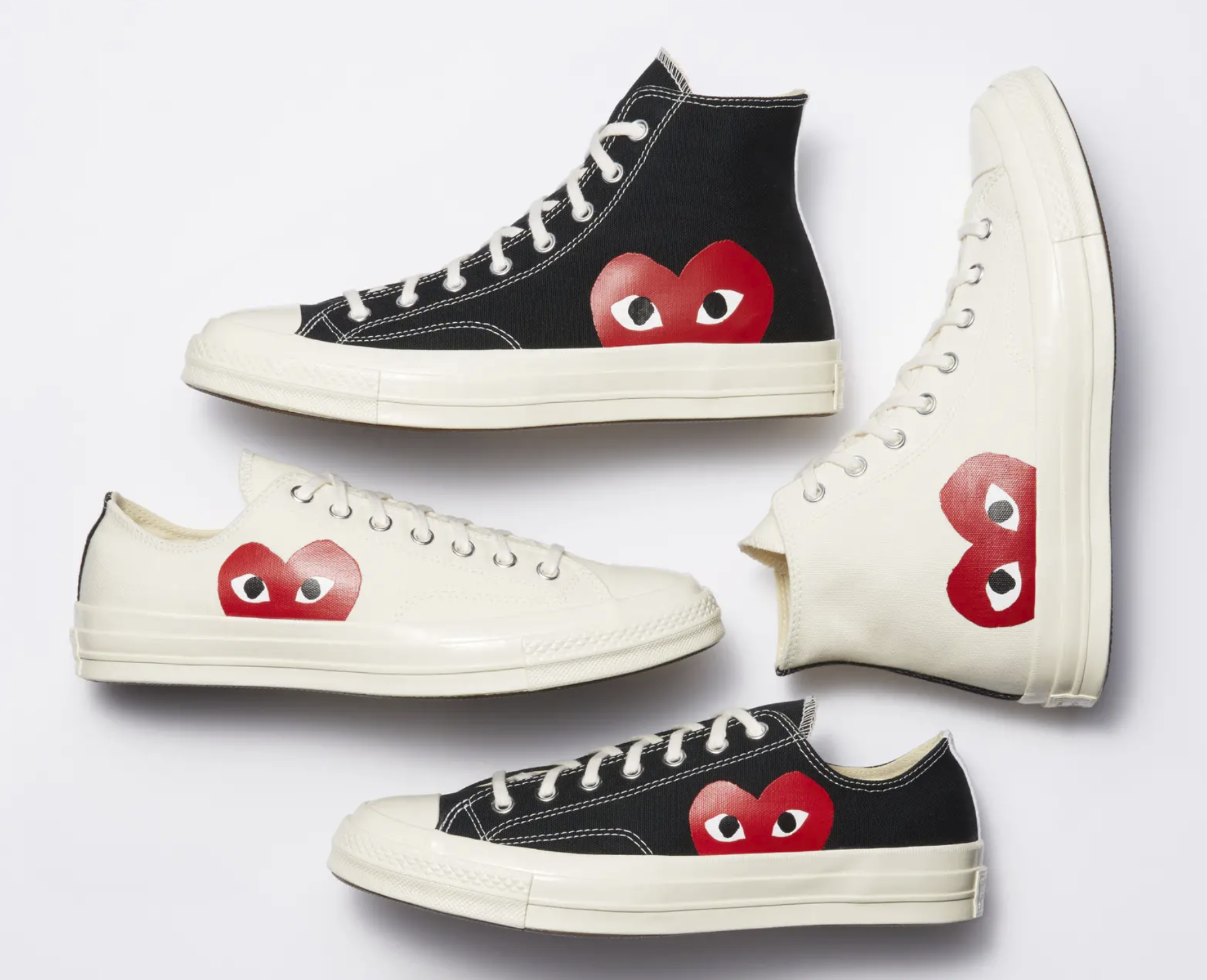 four sneakers laying beside each other. Two are white with a red heart design with eyes drawn on it (one low-top and one high-top). The other two are the black versions.
