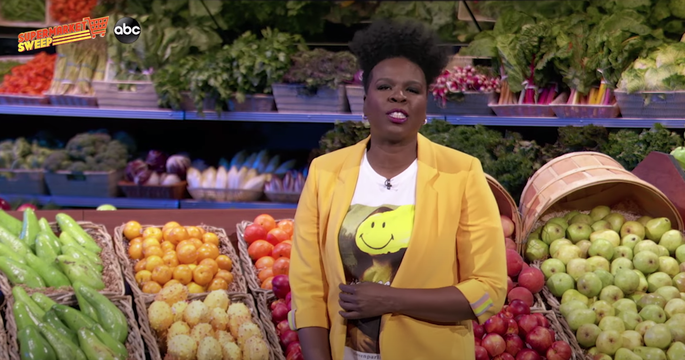 Leslie hosts the show while standing in front of fresh produce featured in the show&#x27;s grocery store set