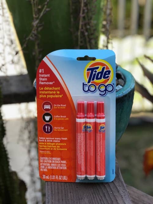 A customer props a pack of three tide stain remover pens on a wooden shelf