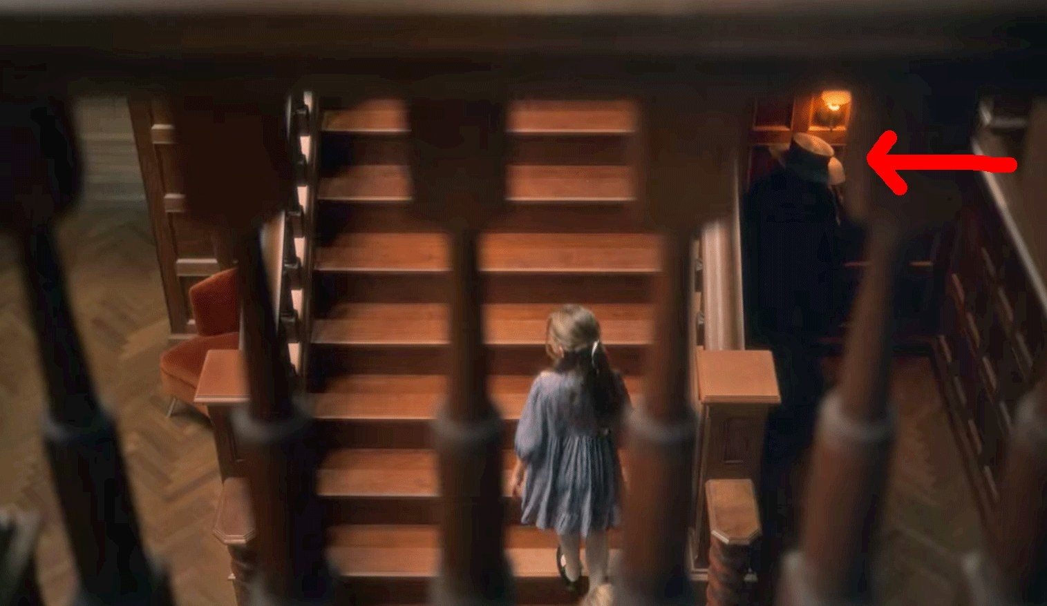 Flora walks up the stairs; a red arrow points to a figure in a hat lurking in the corner below the stairs