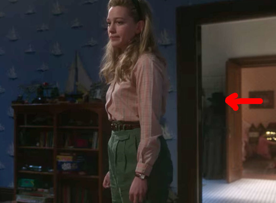 Dani standing in Miles' room; a red arrow points to a shadowy figure seen through the doorway behind her