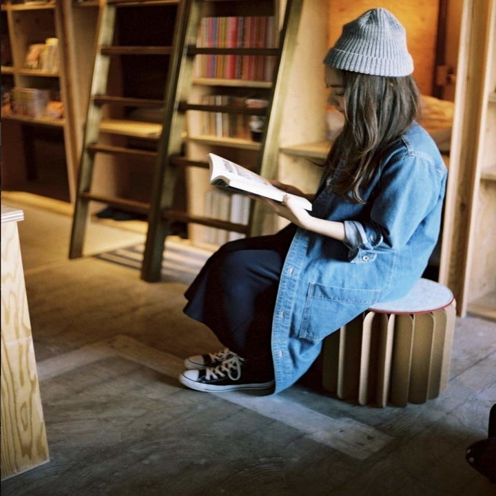 A person sitting on the foldable stool in a library.