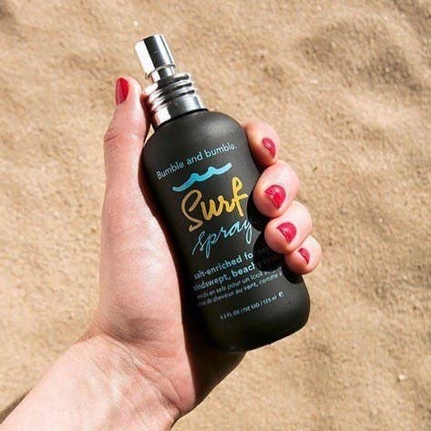 A hand holding a bottle of the spray on the sand