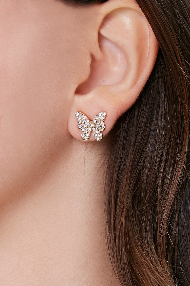 model ear wearing a butterfly stud earring which is gold and has rhinestones on it