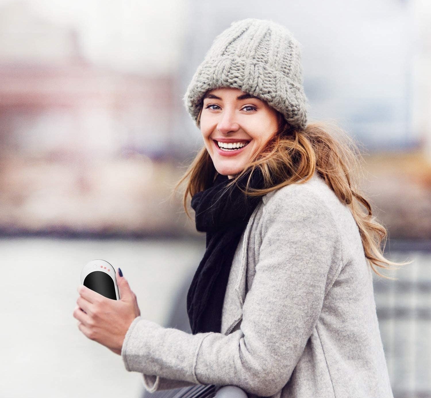 Model smiling holding the Infray hand warmer in their left hand while outside on a chilly day 