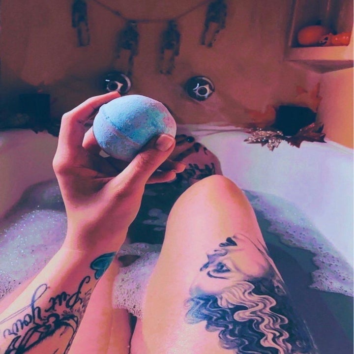 A reviewer holding a bathbomb while relaxing in a colorful bath